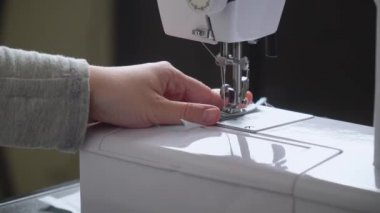 Kadın beyaz koruyucu bir maske dikiyor. Evde pamuk kumaş maskesi yapmak, virüs koruması.