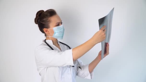 Ung kaukasisk läkare i skyddsmask undersöka röntgen av lungor, hålla den i händerna inomhus. Specialist hålla transparent bild av bröstet i armar, och noggrant forskar det — Stockvideo