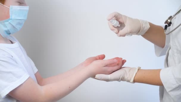 Un médico femenino desinfecta las manos de un niño pequeño con un aerosol antiséptico. Protección Covid-19. Detener coronavirus — Vídeo de stock