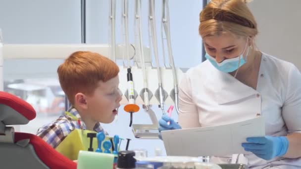 La dentista escribe en una tarjeta médica los síntomas de un paciente varón. Odontología pediátrica — Vídeo de stock