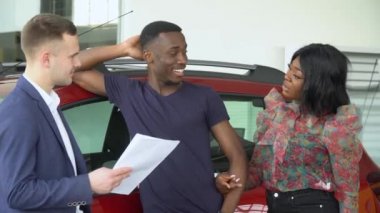 Genç yakışıklı araba satıcısı araba galerisindeki Afrikalı Amerikalı müşterilerine bir şey açıkladı. Özelliklerini açıklıyor.