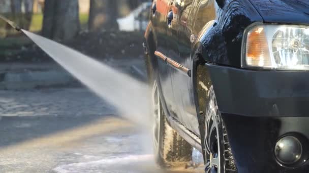 Muž umývá stroj vysokotlakým zařízením. Proud vody s vysokým tlakem spláchne špínu z auta. Samoobslužná myčka aut — Stock video