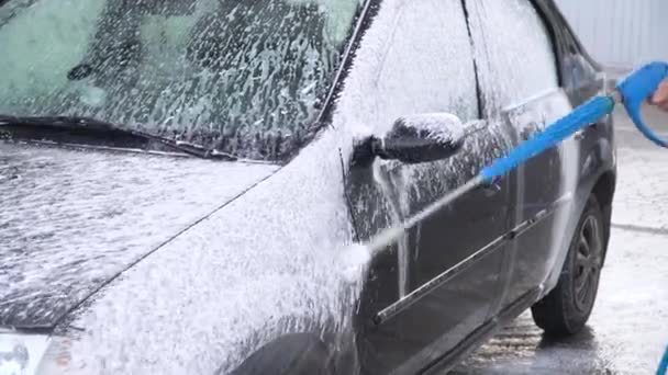 Ένας άνθρωπος στην υπηρεσία αυτοκινήτων πλένει ένα αυτοκίνητο στο suds από σωλήνες νερού — Αρχείο Βίντεο