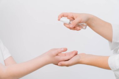 Bir kadın doktor, küçük bir çocuğun ellerini antiseptik spreyle dezenfekte ediyor. Covid-19 koruması. Koronavirüsü durdurun.
