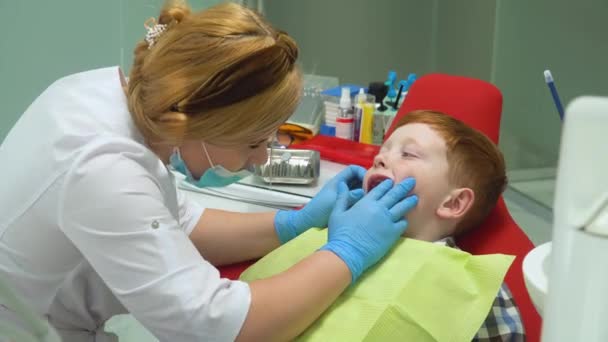 Feliz chico pelirrojo en recepción en el dentista en silla dental. Odontología pediátrica — Vídeo de stock