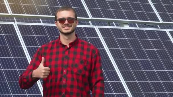 Retrato de um jovem engenheiro bem sucedido no fundo de uma usina solar. Um engenheiro verifica painéis solares — Vídeo de Stock