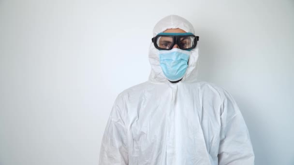 El virólogo está tejiendo en ropa protectora durante la pandemia del coronavirus, retrato. Traje, máscara, guantes y anteojos sobre fondo blanco en clínica u hospital — Vídeo de stock