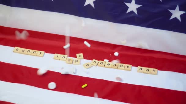 Змішані таблетки падають на прапор США з написом "Щасливий день незалежності". — стокове відео
