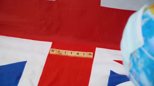 Globe i en skyddande mask med brittisk flagga i bakgrunden. Planet och Storbritannien i karantän — Stockvideo