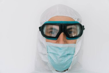 Virolog, koronavirüs salgını sırasında koruyucu giysiler giyip portre yapıyor. Klinikte ya da hastanede beyaz arkaplanda takım elbise, maske, eldiven ve gözlük