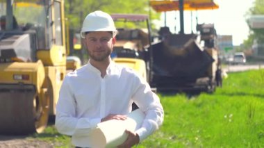 Tamirat müdürünün portresi bir yol inşaatının arka planıyla karşılaştırılır.