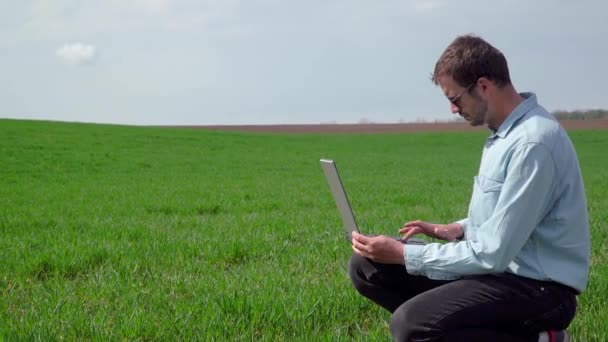 Farmář s laptopem kontroluje růst pšenice. Čerstvé pole zelené pšenice — Stock video