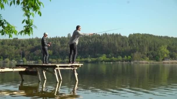Двое мужчин рыбачат на озере. Крутящаяся хищная рыба. Рыбак бросил удочку в озерную или речную воду — стоковое видео