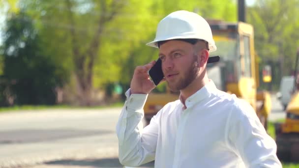 Manager van de reparatie werkt tegen de achtergrond van een weg bouwplaats praten aan de telefoon. Wegenreparatieconcept — Stockvideo