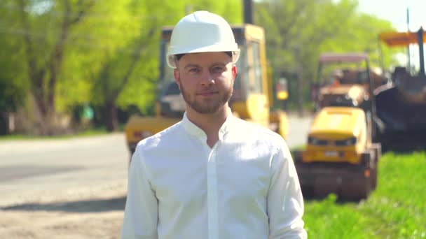 Manager van de reparatiewerkzaamheden in een witte helm op de achtergrond van speciale wegapparatuur — Stockvideo