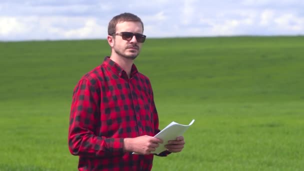 Közelkép egy mosolygós gazdáról, aki a zöld búzamezőn áll és a kamerába néz. — Stock videók