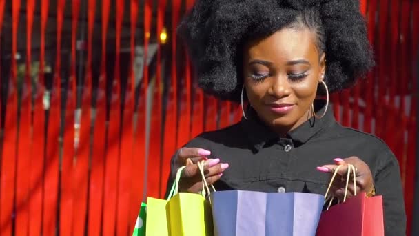 Chica africana feliz con bolsas de compras sobre un fondo rojo. Concepto de compras — Vídeos de Stock