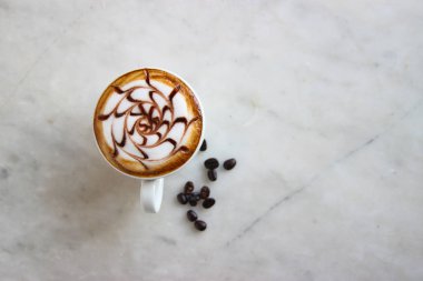 Top view, closed up hot caramel latte with milk steam pattern art, decorate with beans and green leaves.