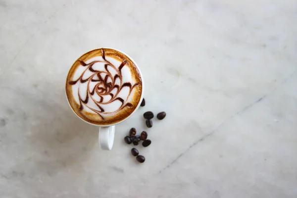 Top view, closed up hot caramel latte with milk steam pattern art, decorate with beans and green leaves. — Stok fotoğraf