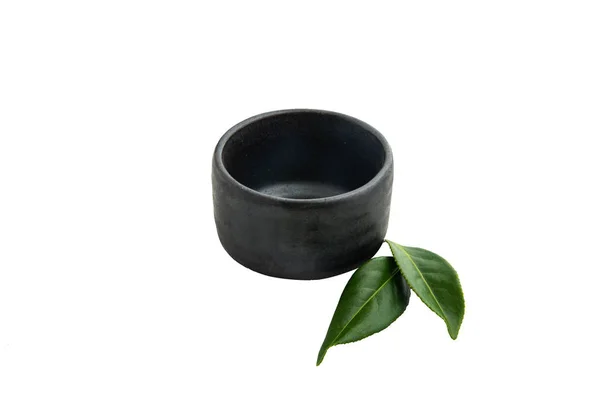 Isoler un bol de céramique foncée avec de petites feuilles de thé vertes sur fond blanc à côté.. — Photo