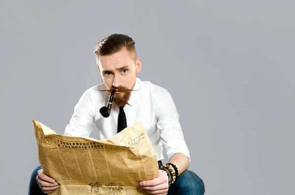 Stylish guy with a pipe reads old newspaper