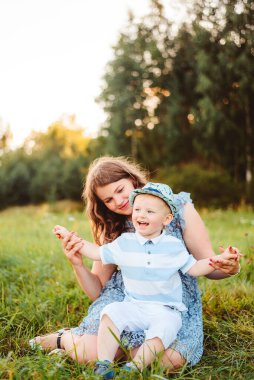 Anne ve oğlu doğada çimenlerde oturup oynuyorlar. Yaz akşamı ve gün batımı.