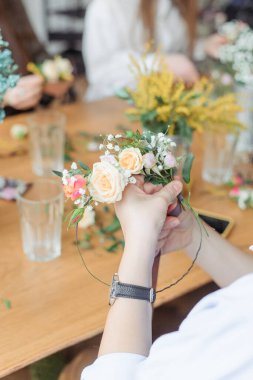 Atölye çiçekçisi, buketler ve çiçek düzenlemeleri yapıyor. Kız kafasında çelenk yapıyor. Bitki ve çiçeklerle çelenk dokuma işlemi. Çiçekçilerin yakın çekim dersi. Boşluğu kopyala