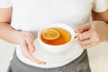 Beyaz bardakta limonlu siyah çay bir kızın elinde, ev eşyaları. Hastane karantinası. Önleme