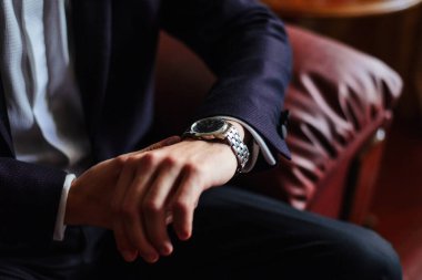 Karanlık bir iç mekandaki bir adam, gümüş bir bilek saatinde saatin kaç olduğunu izler. Düğün sabahı, damat..