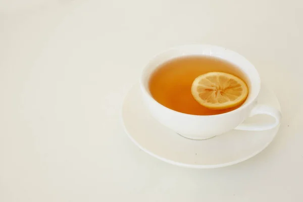 白テーブルの上の白いカップにレモンと黒茶と背景 — ストック写真