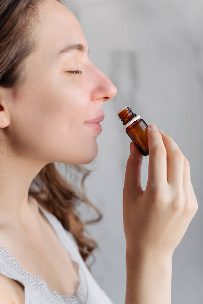 A young girl sniffes essential aromatic oil. Bright home bathroom. Relax, aromatherapy, aromapsychology.
