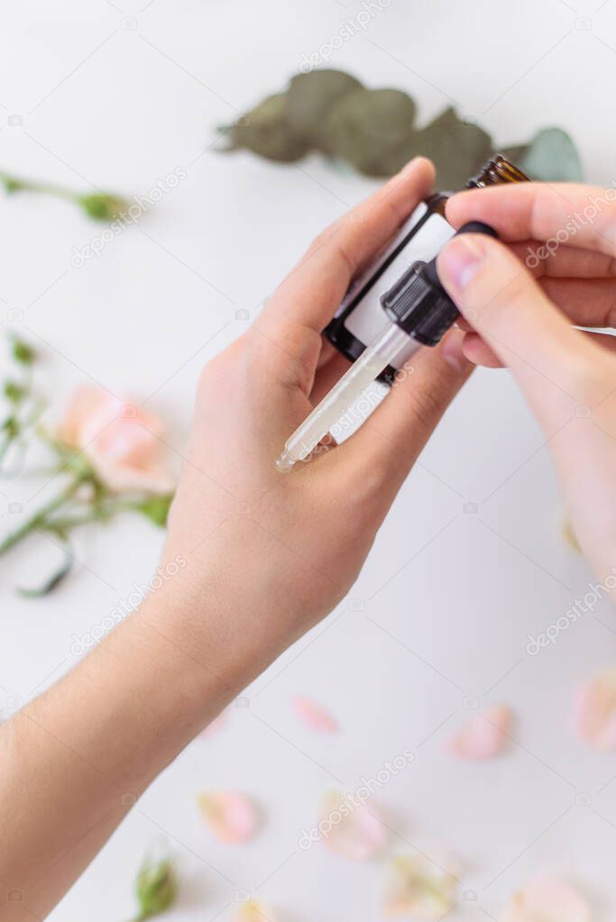 Applying serum to the hand to care for the face. Bright background with rose flowers and eucalyptus leaves. Natural vegan cosmetics. Close up. Hyaluronic serum, rejuvenation, problematic skin and acne