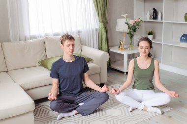Genç çift - erkek ve kadın - evde spor yapıyor. Spor giysisi. Yoga, pilates, nefes alma, meditasyon Ardha Padmasana egzersizi, yarım Lotus pozu Mudra hareketi. Sabah vardiyası, egzersiz, yaşam tarzı. İyi olmak, sağlık kavramı..