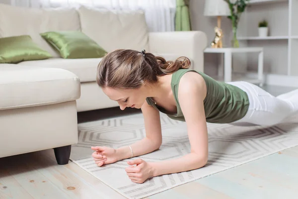 A slim girl does sports at home. White leggings and green top. Yoga, pilates, plank. Morning charging, workout, lifestyle.