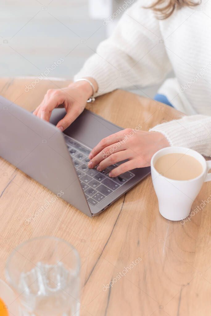 Woman is typing on keyboard of laptop or notebook at home freelance, check electronic mail, get some information for shopping online or operate of banking on web. Cup of coffee.