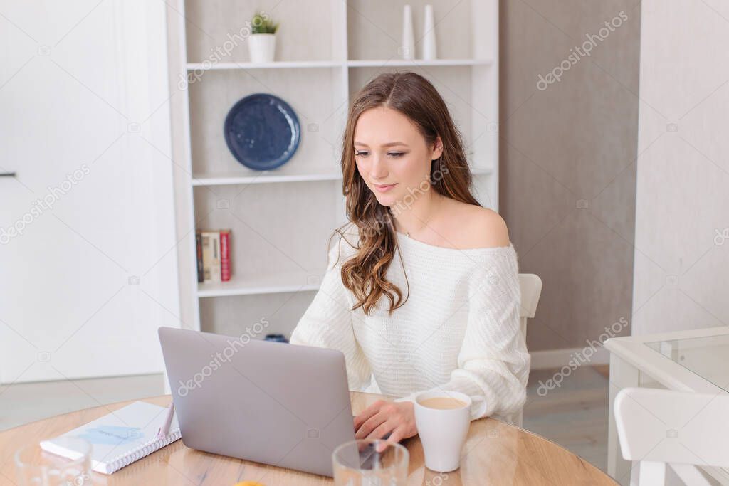 Young beautiful woman works for a laptop computer from a home with a laptop as a freelancer. Weekend at house.