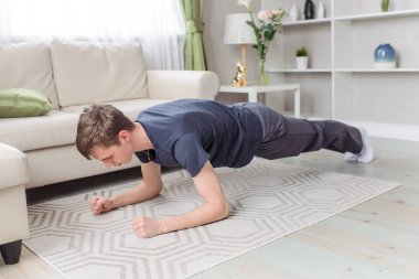 Genç adam evde spor yapıyor. Koyu mavi giysi. Yoga, pilates, tahta. Sabah şarjı, egzersiz, yaşam tarzı.