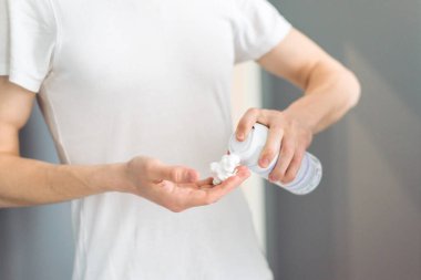 Beyazlar içindeki genç bir adam gün ışığı banyosunda eline köpük sürüyor. Kapat..