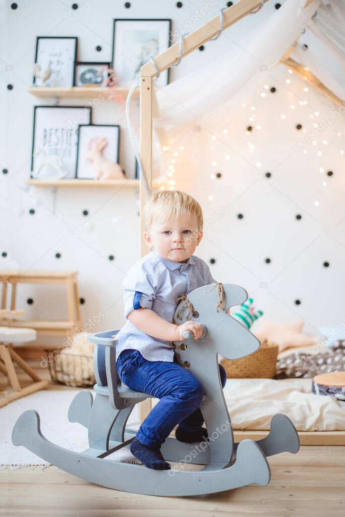 A little boy rides a toy horse in a children 's cosy room.