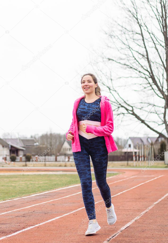 A young girl sports in the open air of the stadium. A woman runs down the road and smiles. Healthy lifestyle.