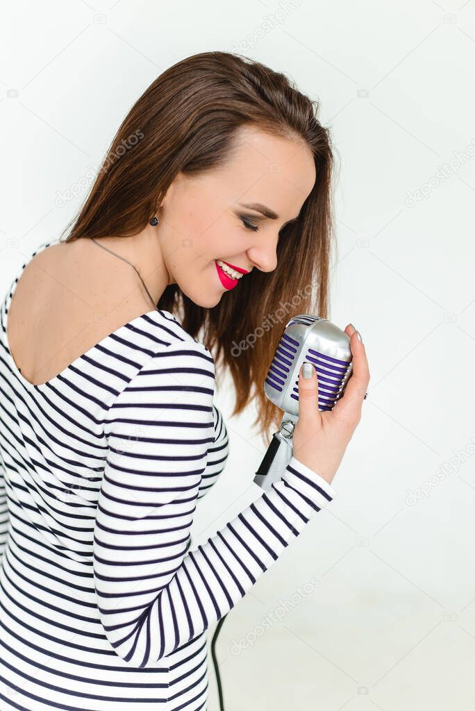 A girl with red lipstick holds a retro microphone and sings on white background. The isolated portrait.