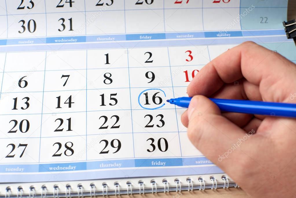 hand marks date on the calendar in blue