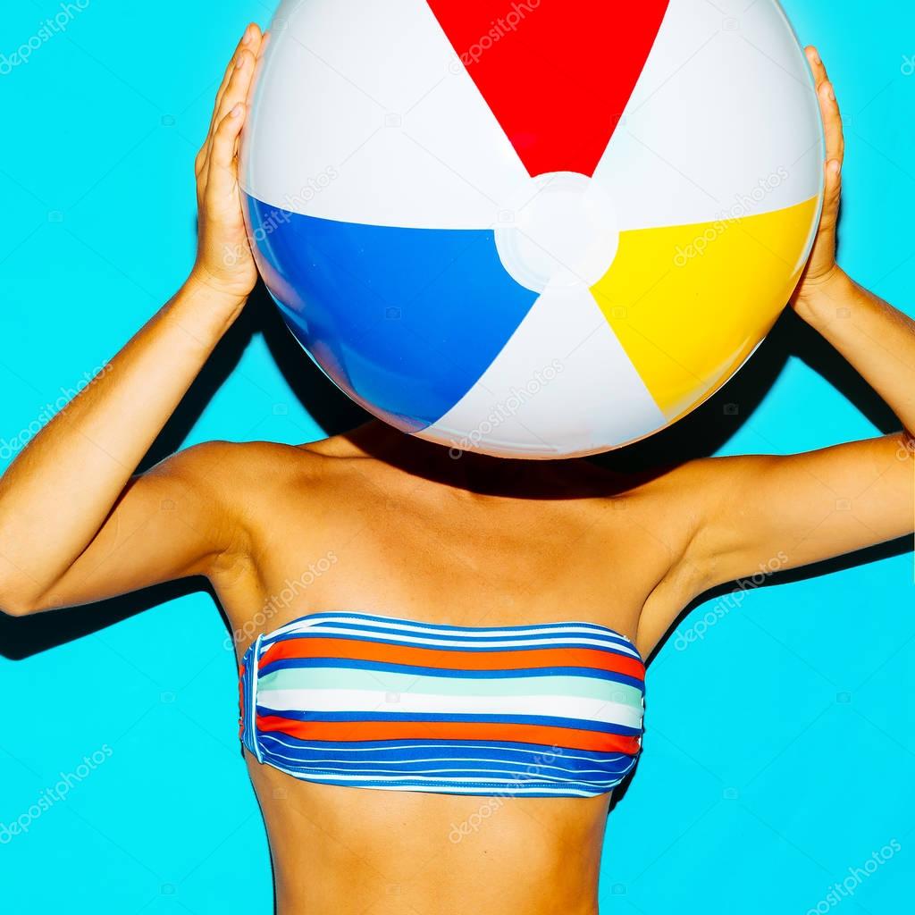 Tanned girl in a stylish bikini and with a beach ball. Beach sty