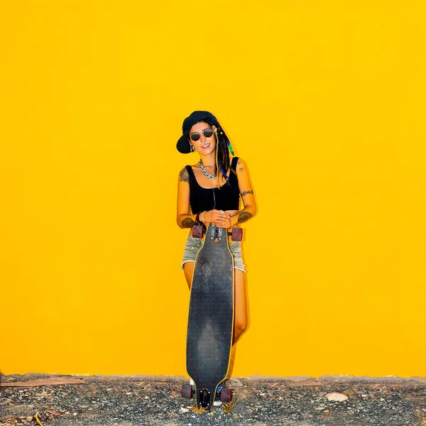 Güzel genç kız sarı arka plan duvar bir kaykay ile — Stok fotoğraf