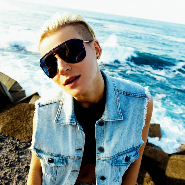 Stijlvolle blonde in een denim jasje en trendy zonnebril. Oceaan — Stockfoto