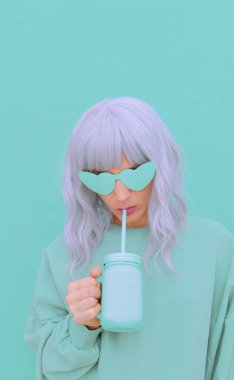 Estetik sarışın kız şık aksesuarlar, güneş gözlüğü ve taze meyve püresi takıyor. Nane monokrom renk tasarımı