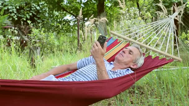 Muž v houpací síti, přehrávání na telefonu — Stock video