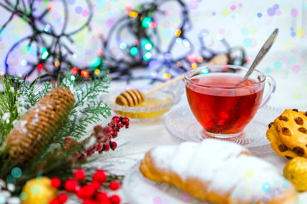 Рождественский чай в стеклянной чашке. композиция с печеньем, сосновыми ветвями, шишками на фоне гирлянд на деревянном столе — стоковое фото