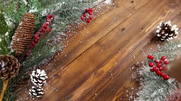 Weihnachten hölzernen Hintergrund mit verschneiten Zweig Draufsicht. die Hände eines jungen Mädchens legen ein Geschenk mit roter Schleife auf den Tisch — Stockvideo