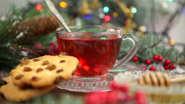 Té de invierno Una taza de té con miel y croissant o galletas, una rama de un árbol de Navidad en la nieve, luces de Navidad — Vídeos de Stock
